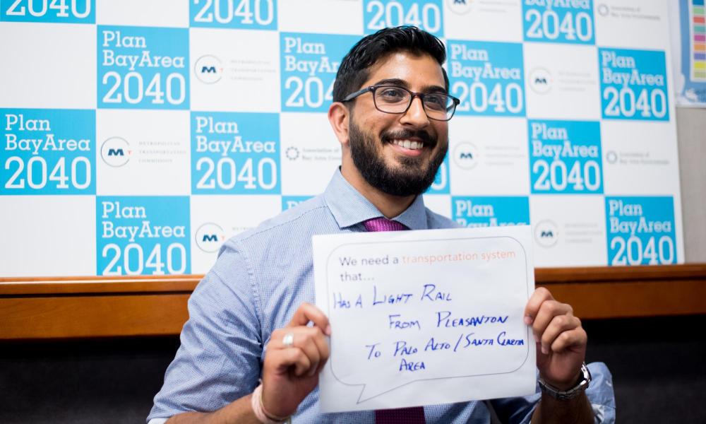 A resident poses for a photo with a sign expressing his thoughts on how to improve the Bay Area's transportation system at the Plan Bay Area 2040 open house in Fremont.