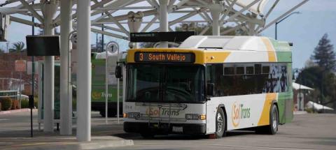 A SolTrans bus sits at a bus stop in the Vallejo Transit Center on a sunny day.