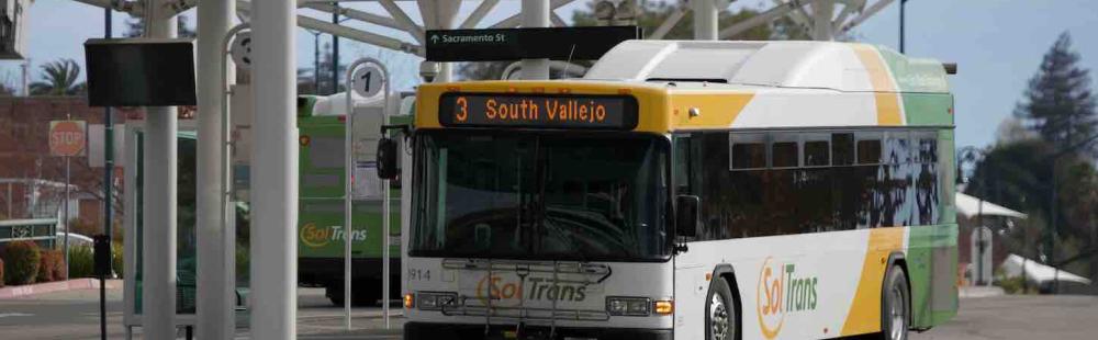 A SolTrans bus sits at a bus stop in the Vallejo Transit Center on a sunny day.